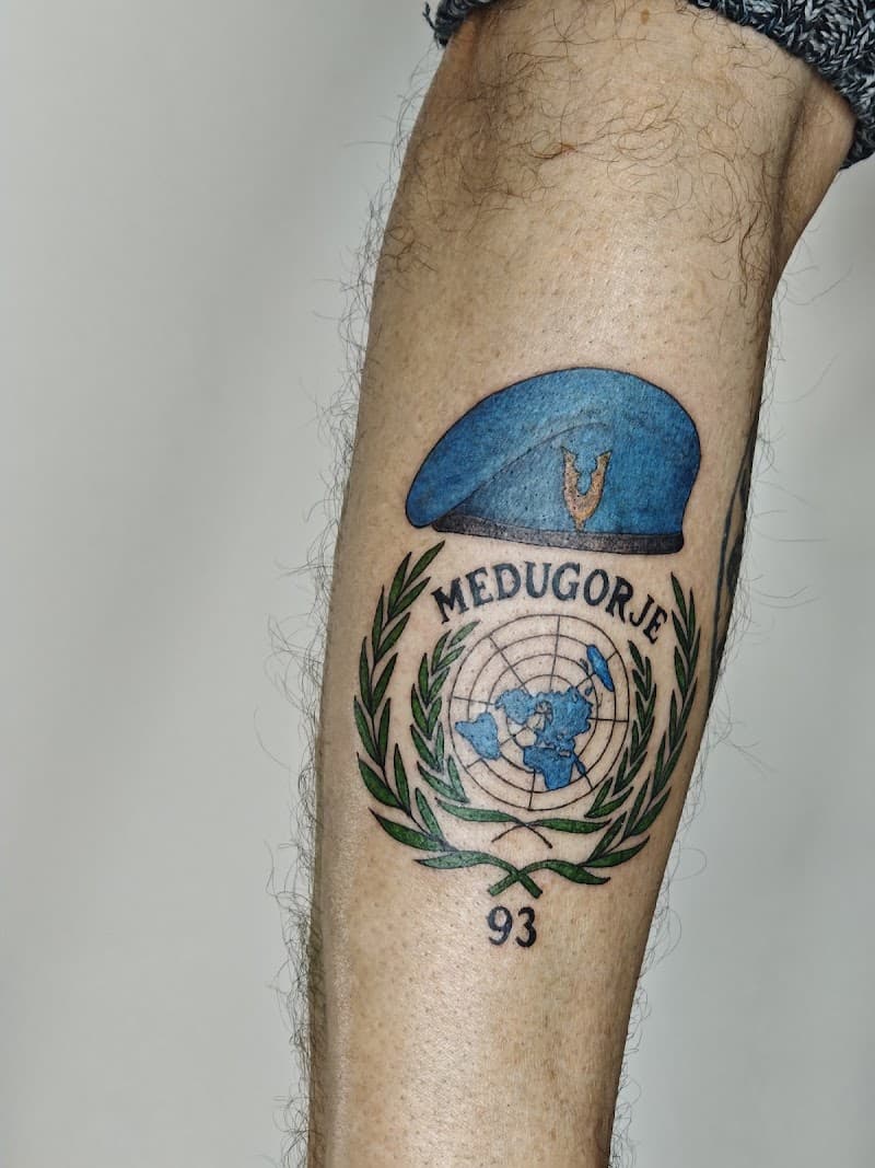 Tattoo van blauwe VN-baret, VN-logo, 'MEDUGORJE' en '93' op onderbeen.