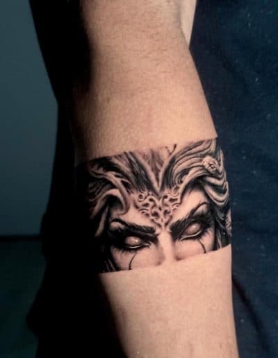 Realistische zwart-wit tattoo van Medusa's ogen en slangenhaar in een band.