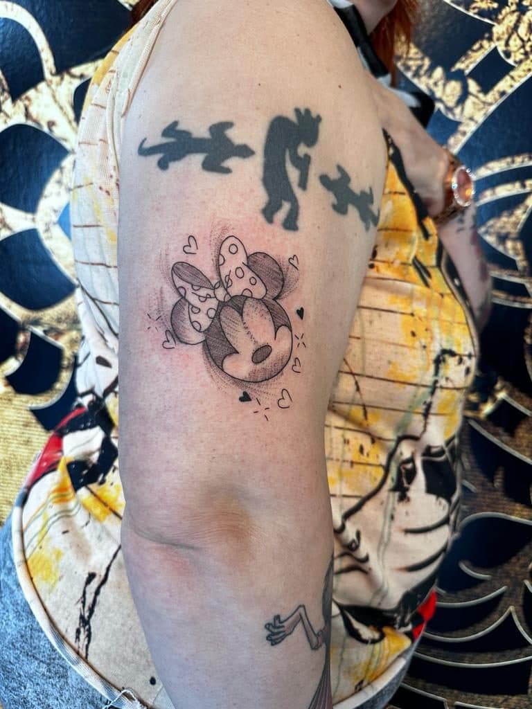 Schetsmatige Minnie Mouse tattoo met hartjes op bovenarm.
