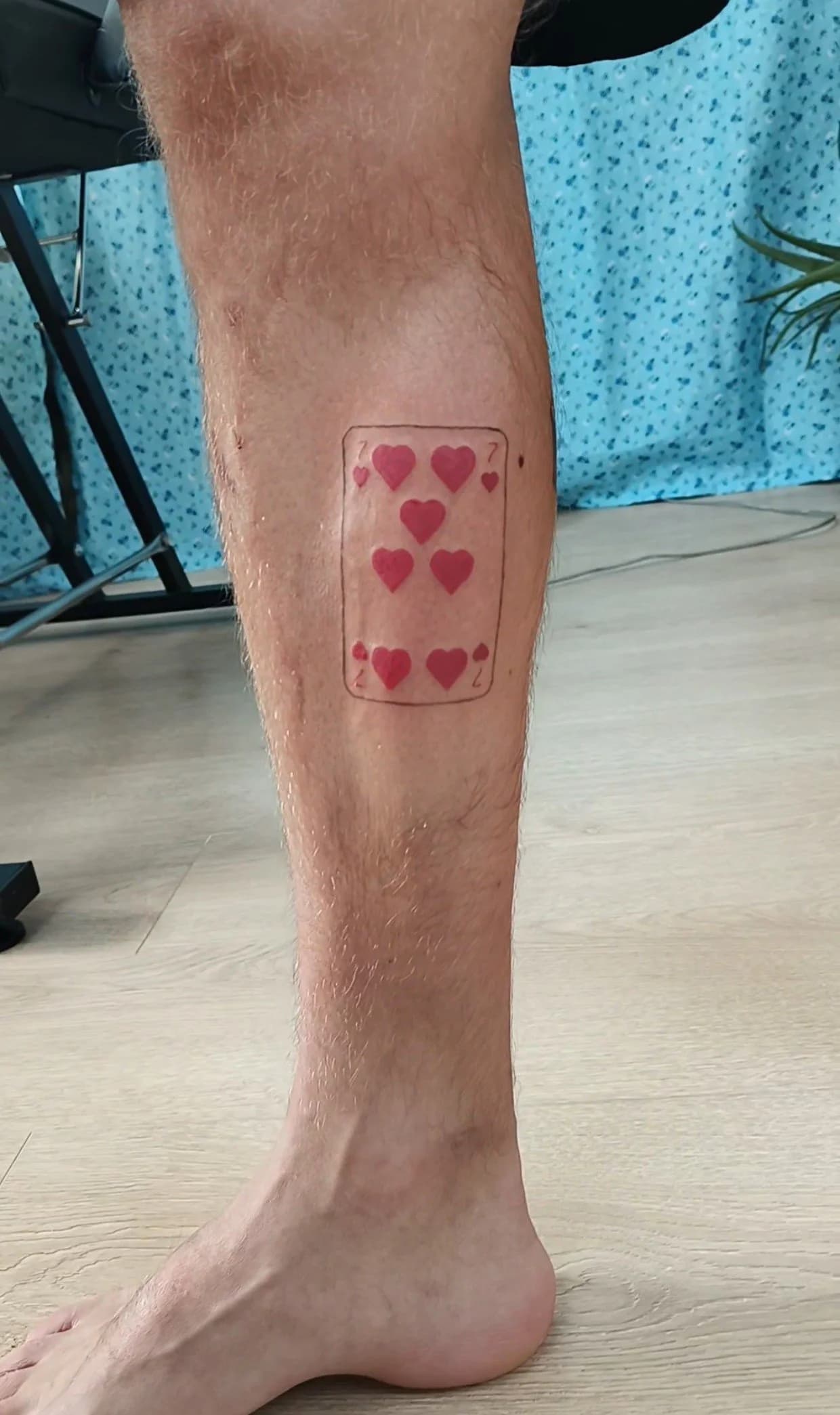Minimalistische harten zeven speelkaart tattoo op het onderbeen.