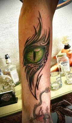 Groen reptielenoog met zwarte tribal-achtige omlijning op het onderbeen.