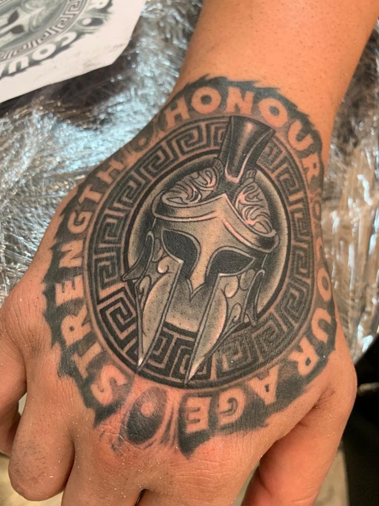 Zwart-wit Spartaanse helm met Griekse rand en tekst 'STRENGTH HONOUR COURAGE' op hand.