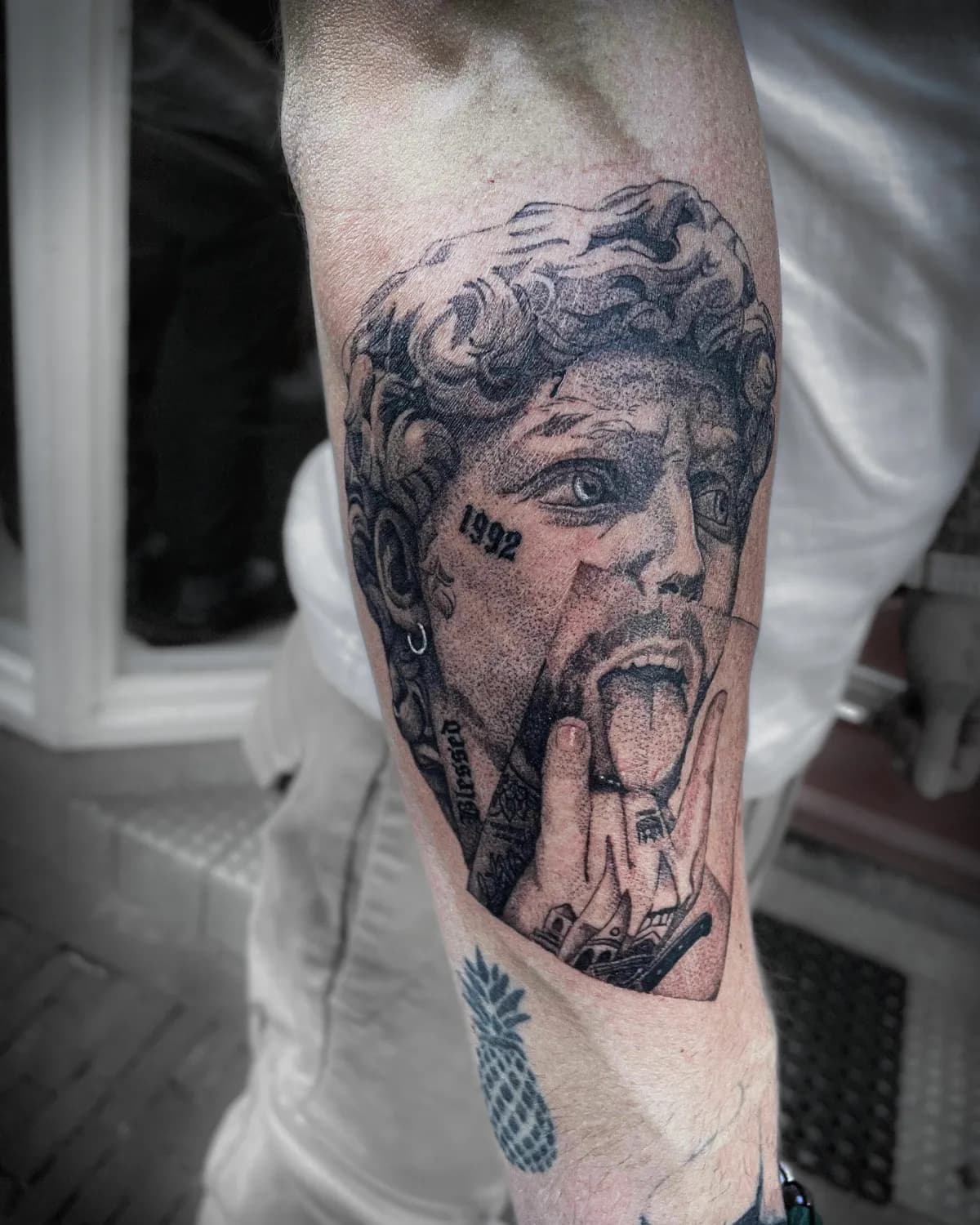 Zwart-wit portret tattoo van man met tong uit en handgebaar, plus ananas.