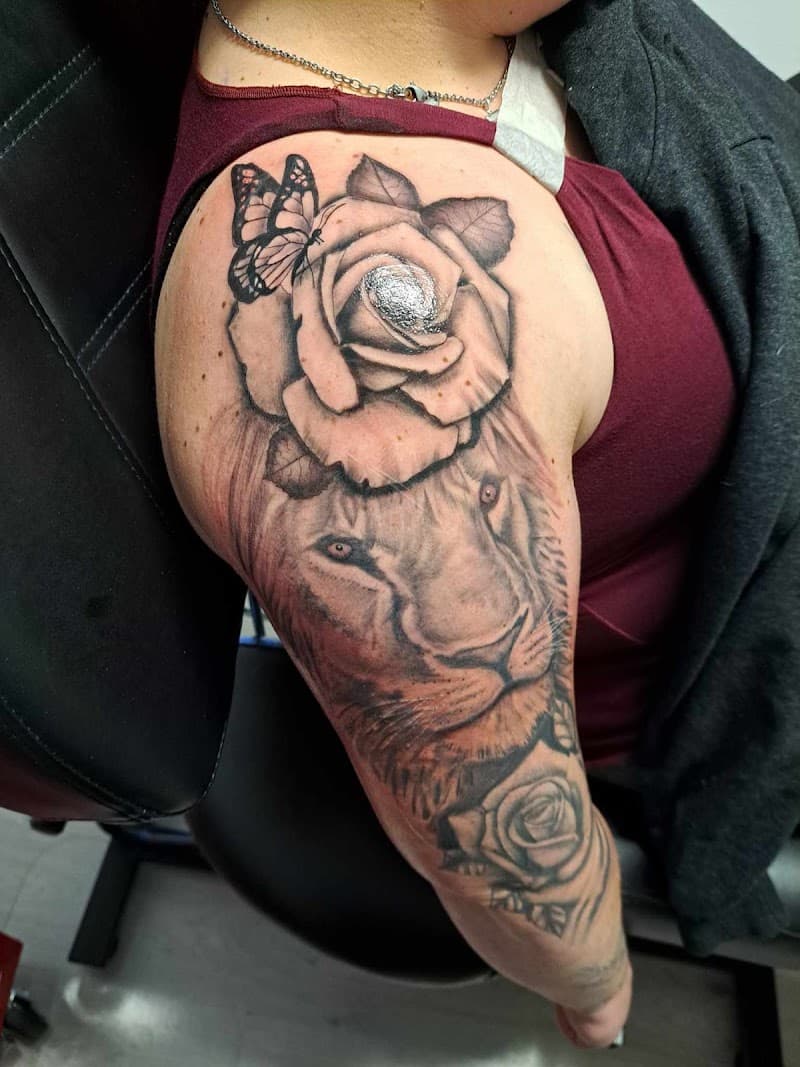 Zwart-wit tattoo van een leeuw met rozen en een vlinder op de bovenarm.