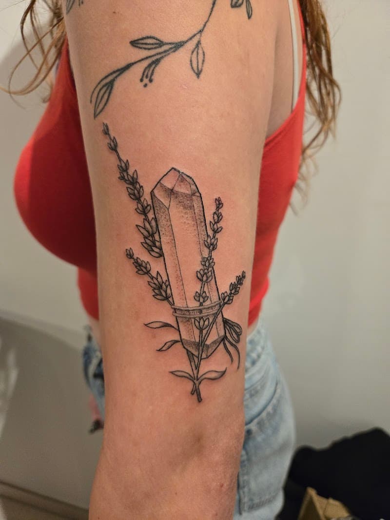 Fineline tattoo van een kristal met lavendel takjes eromheen gebonden.