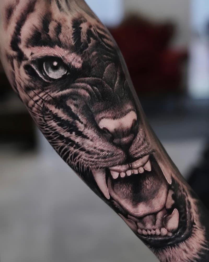 Realistische zwart-wit tattoo van een brullende tijgerkop op de onderarm.