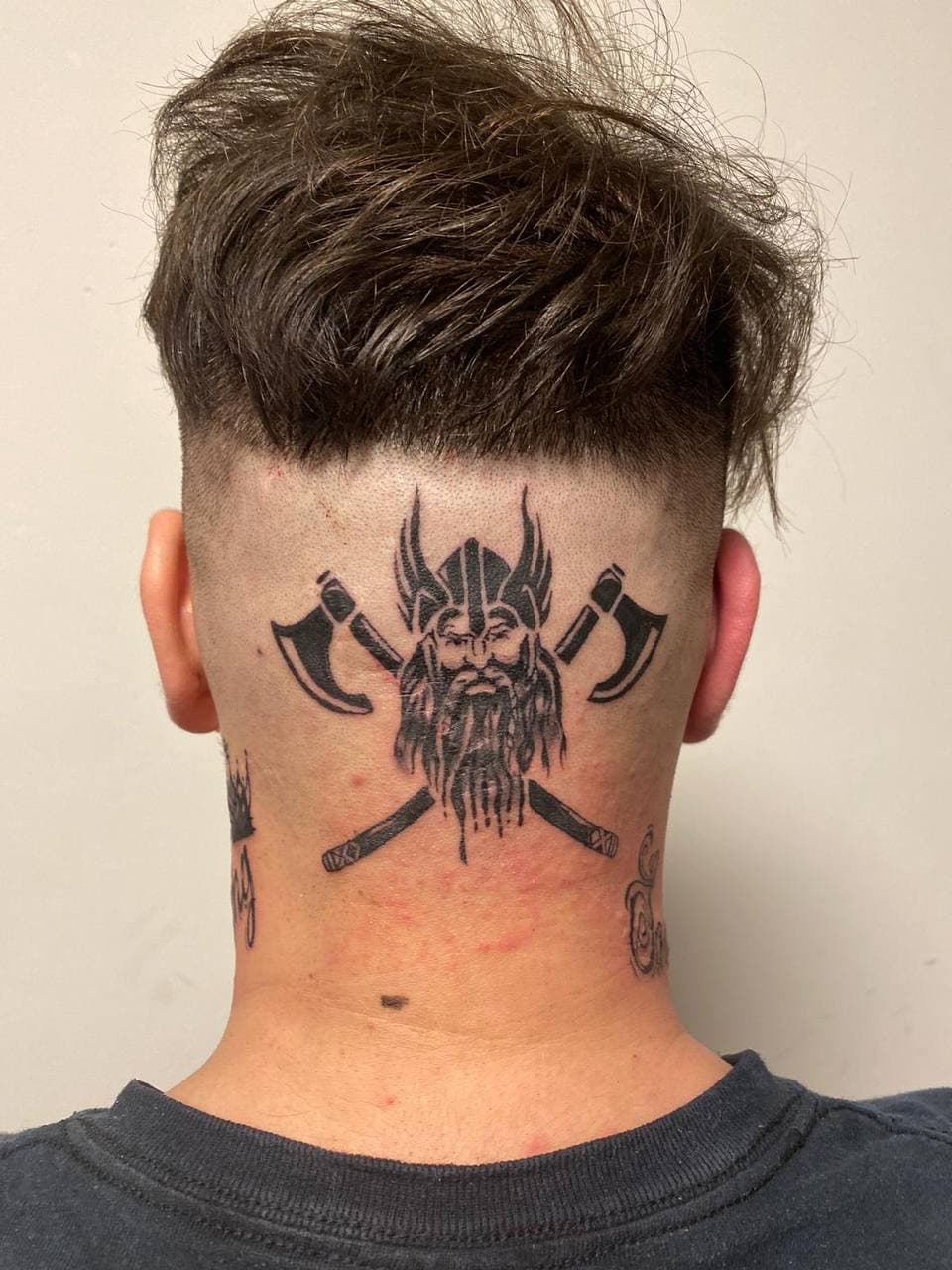 Zwart-wit tattoo van een Vikinghoofd met gekruiste bijlen op het achterhoofd.