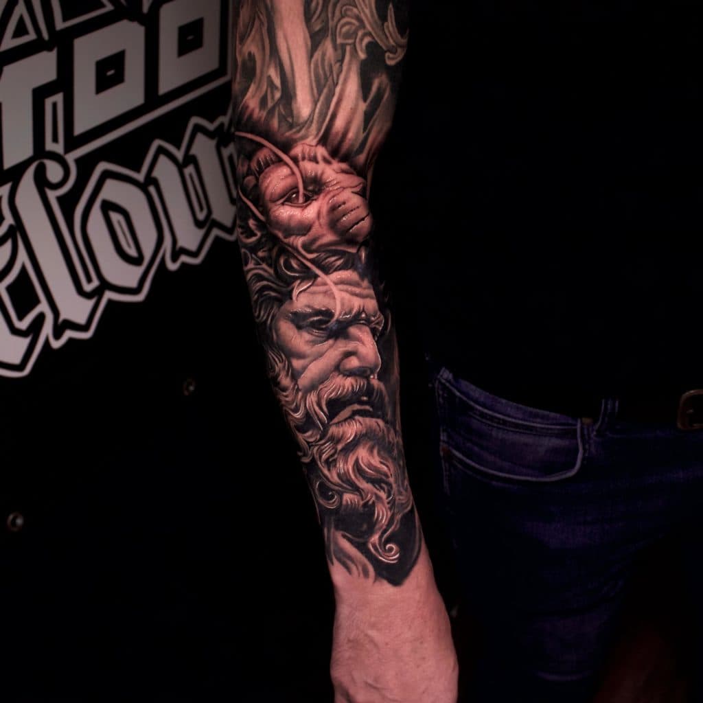 Realistische zwart-wit tattoo van een Griekse god (Zeus/Poseidon) op de onderarm.