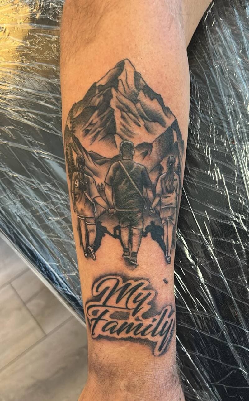 Zwart-wit tattoo van een gezin dat naar bergen loopt met de tekst "My Family".