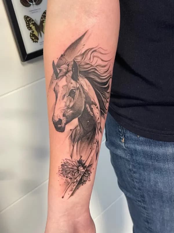 Illustratieve blackwork tattoo van een paardenhoofd met bloem op de onderarm.