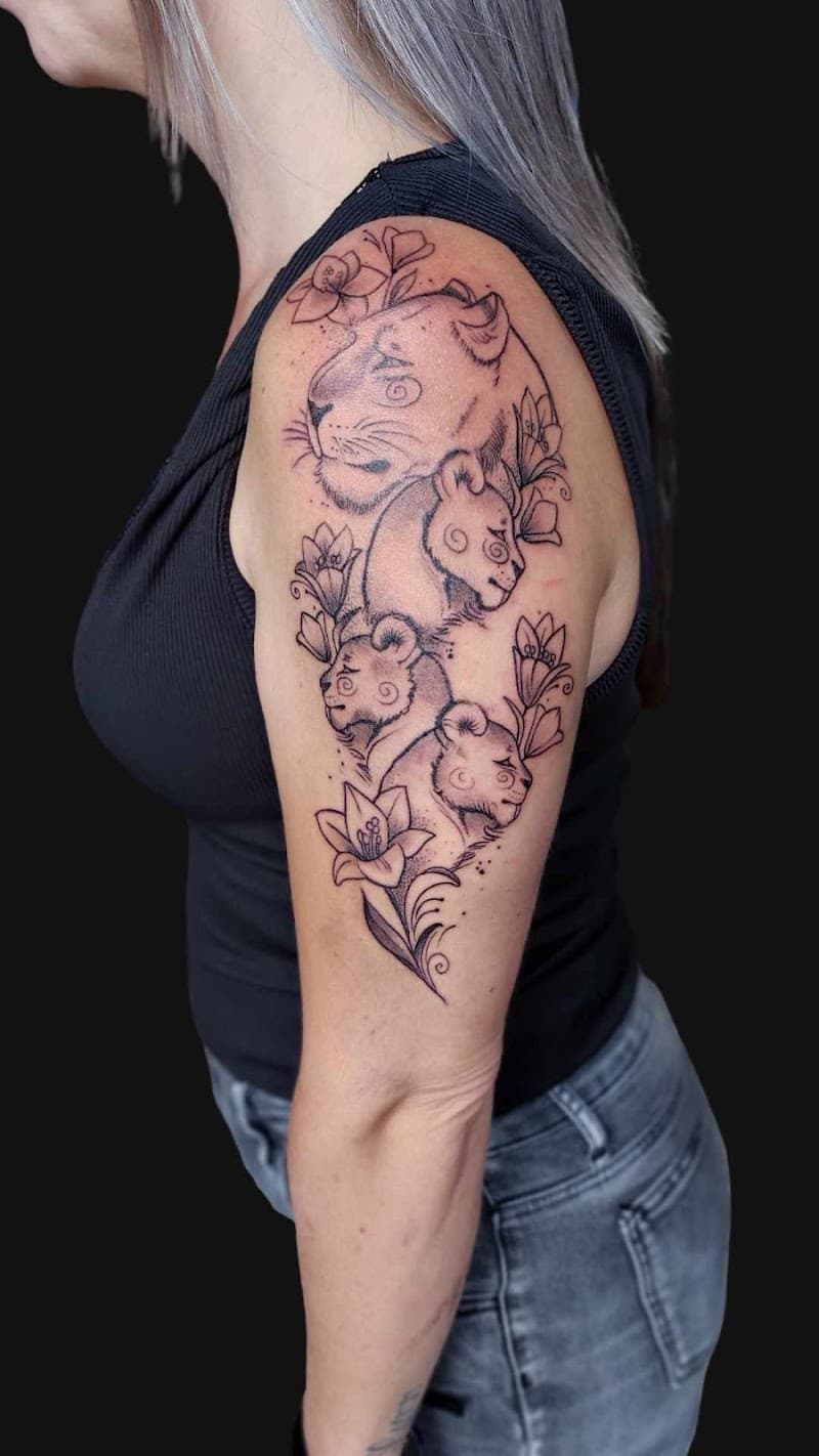 Fineline tattoo van leeuwin met drie welpen en bloemen op bovenarm.