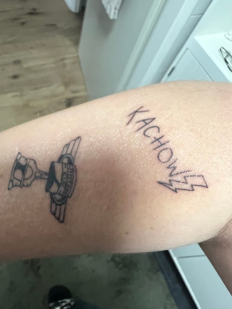 Twee kleine tattoos: Piston Cup trofee en 'KACHOW' met bliksem.
