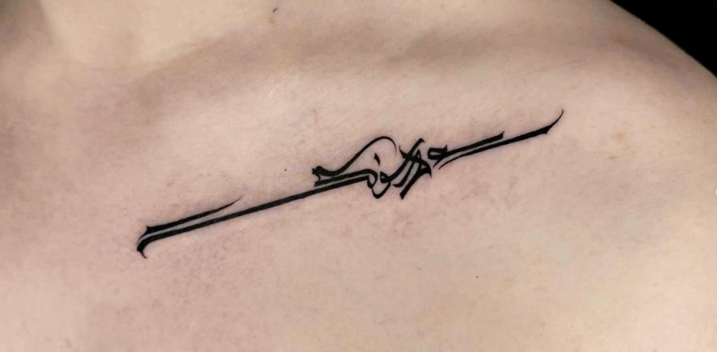 Sierlijke zwarte kalligrafie tattoo op het sleutelbeen.