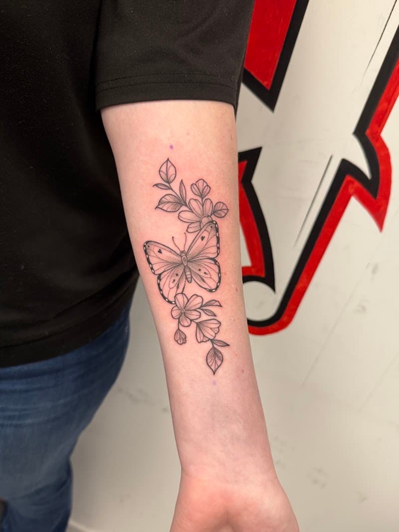 Fineline vlinder met bloemen en bladeren op onderarm.