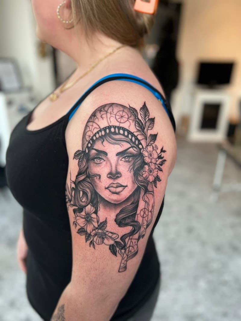 Zwart-wit portret van een vrouw met hoofddoek en bloemen op de bovenarm.