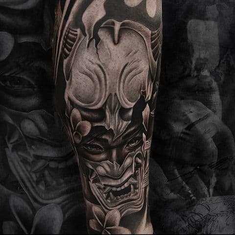 Realistische zwart-grijze Hannya masker tattoo met kersenbloesem op onderbeen.