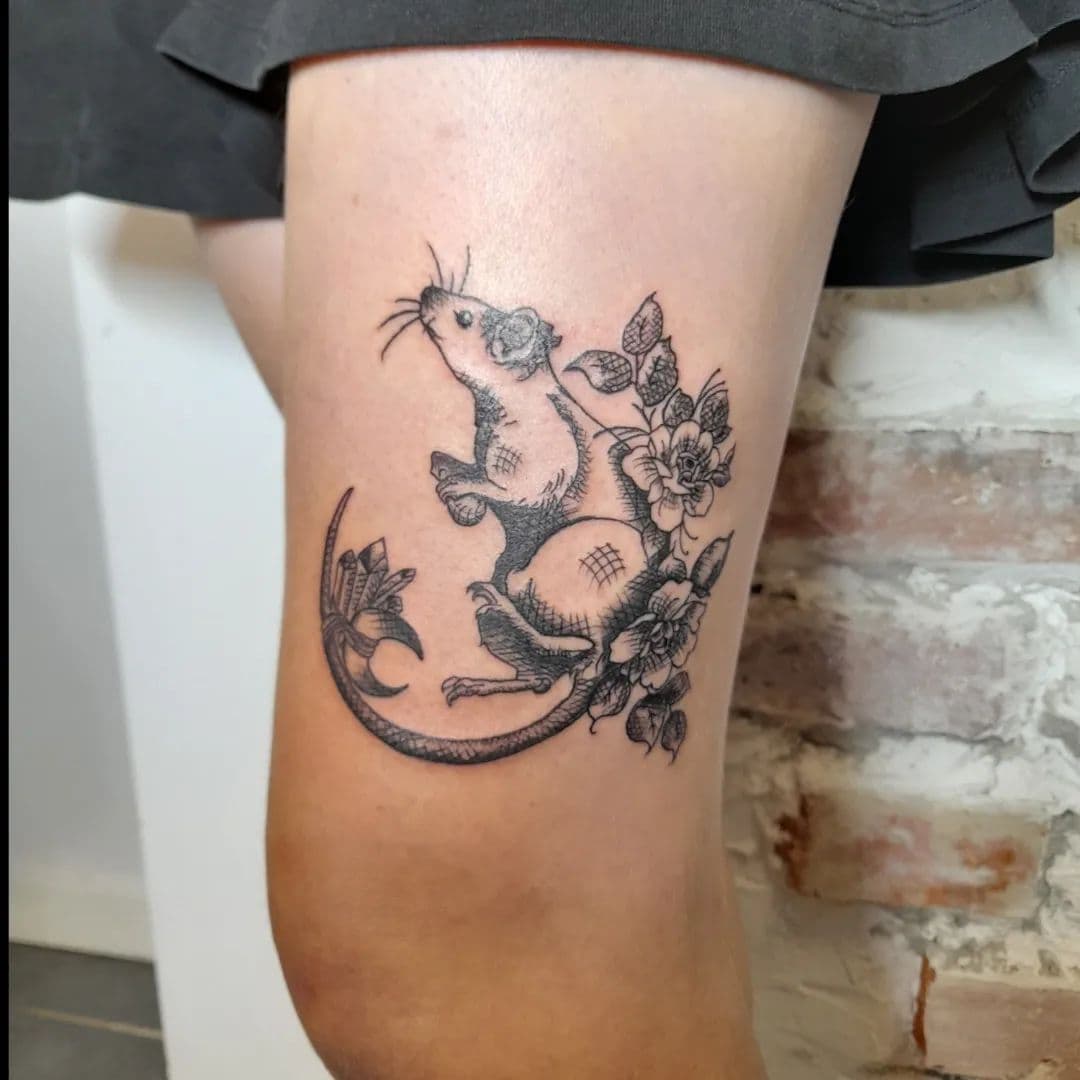 Gedetailleerde gravure-stijl tattoo van een rat met bloemen op het bovenbeen.