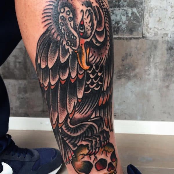 Traditionele tattoo van een adelaar op een schedel op het onderbeen.