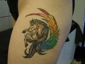 Kleurrijke pegasus tattoo met regenboogvleugel op bovenbeen.