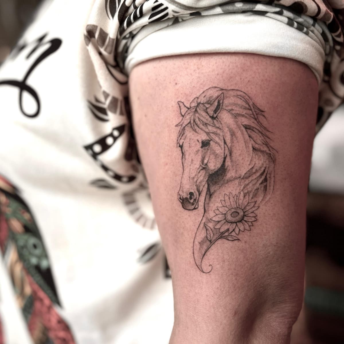Fineline tattoo van een paardenhoofd met een zonnebloem op de bovenarm.