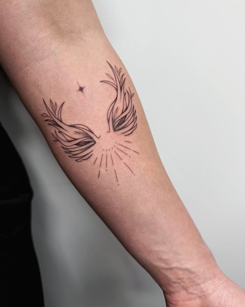 Fineline tattoo van vleugels met bladeren, een ster en stralen op de onderarm.