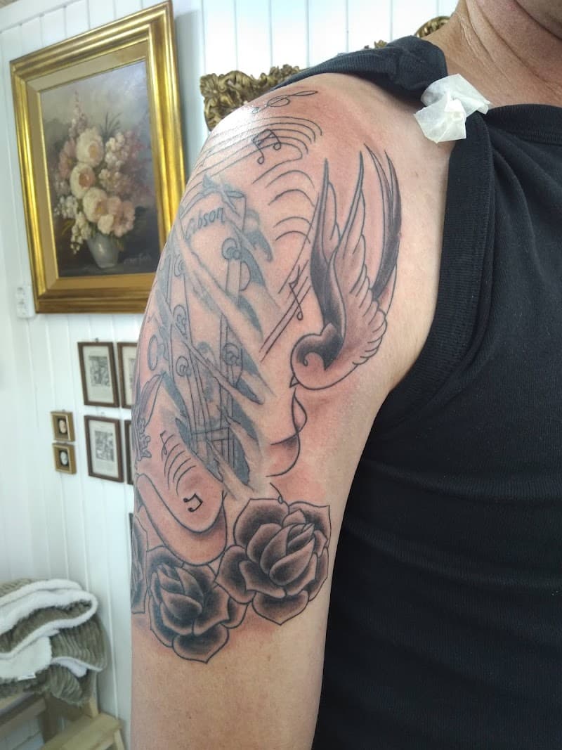 Zwaluw, rozen, muzieknoten en gitaar op bovenarm.