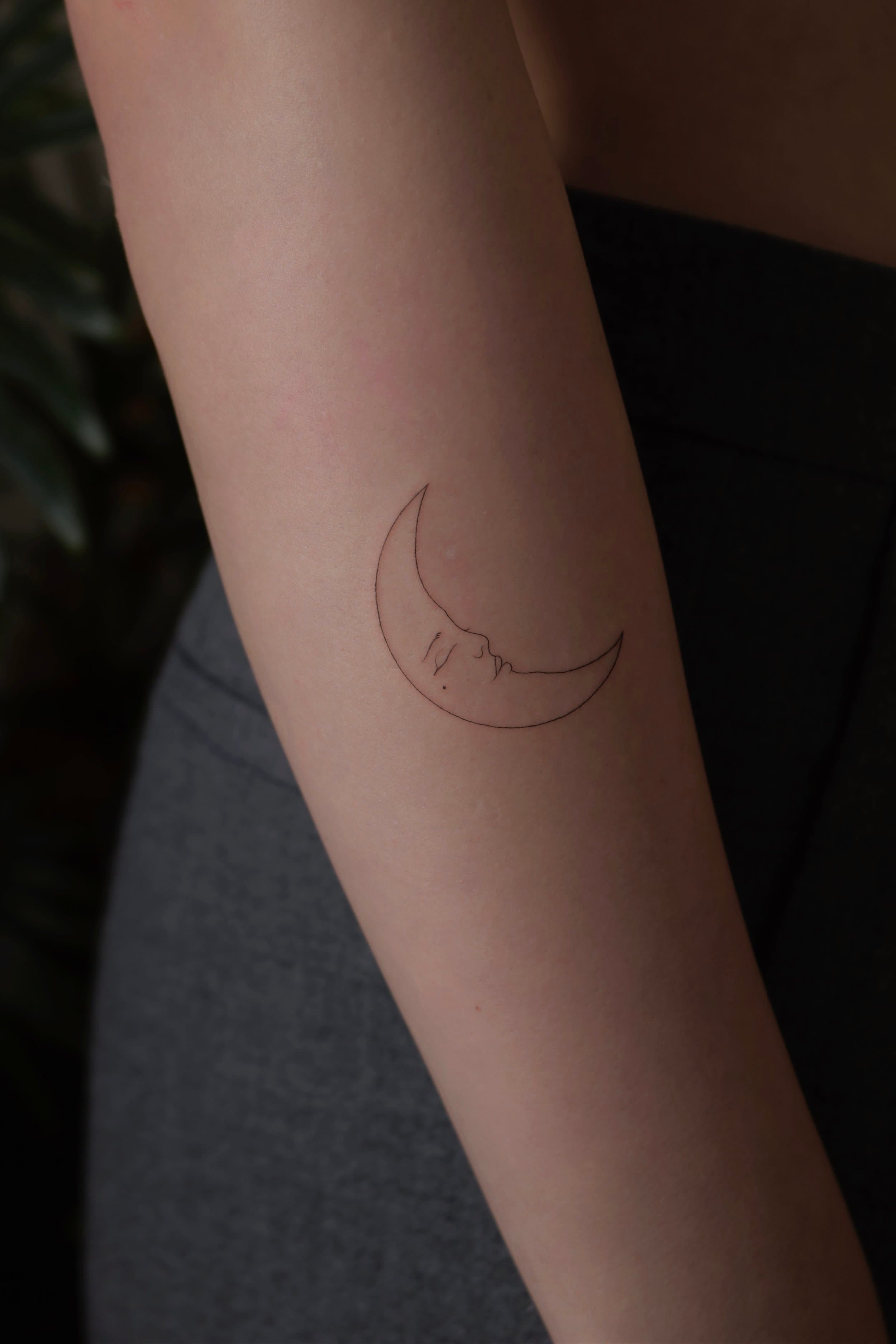 Minimalistische fineline maan met slapend gezicht op onderarm.