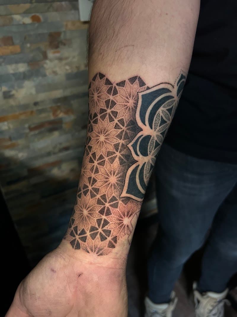 Geometrische dotwork tattoo met mandala patroon op onderarm.