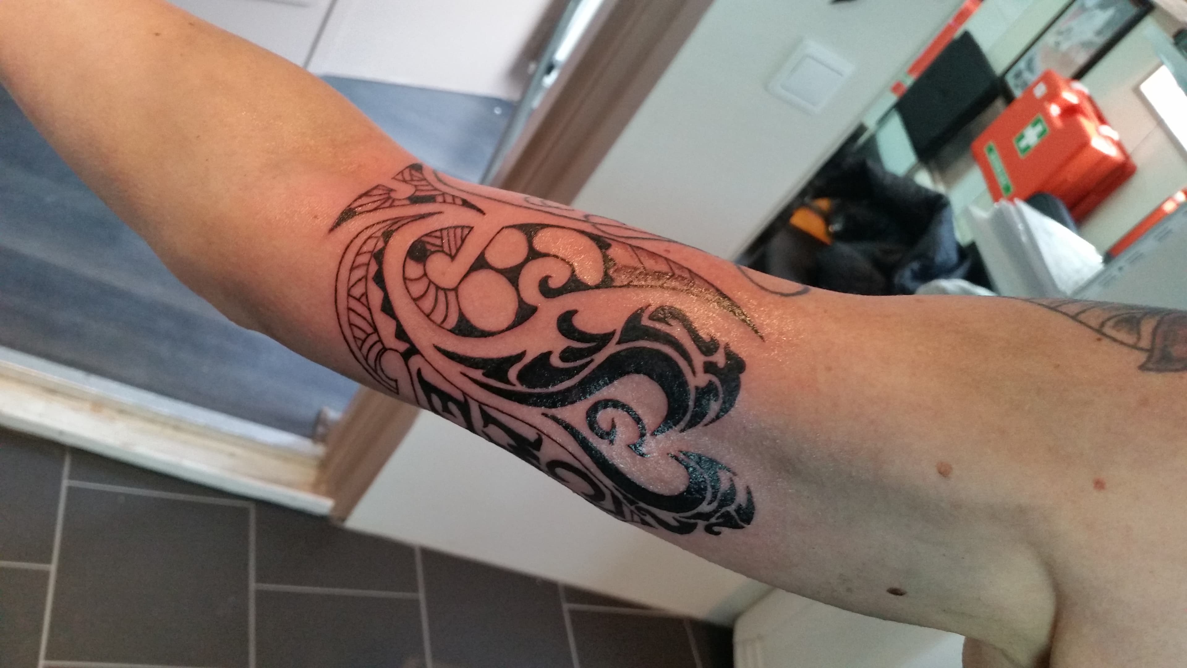 Zwarte tribal tattoo op bovenarm met abstracte vormen.