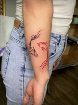 Twee fineline koi vissen, één zwart en één rood, op de onderarm.