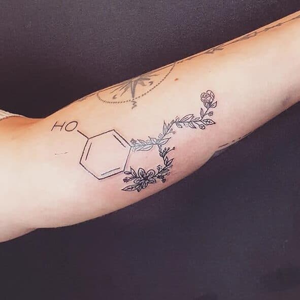 Fineline tattoo van serotonine molecuul met bloemen op bovenarm.