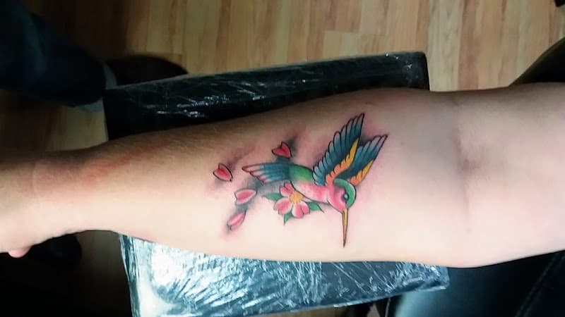 Kleurrijke kolibrie met bloem en blaadjes op onderarm.