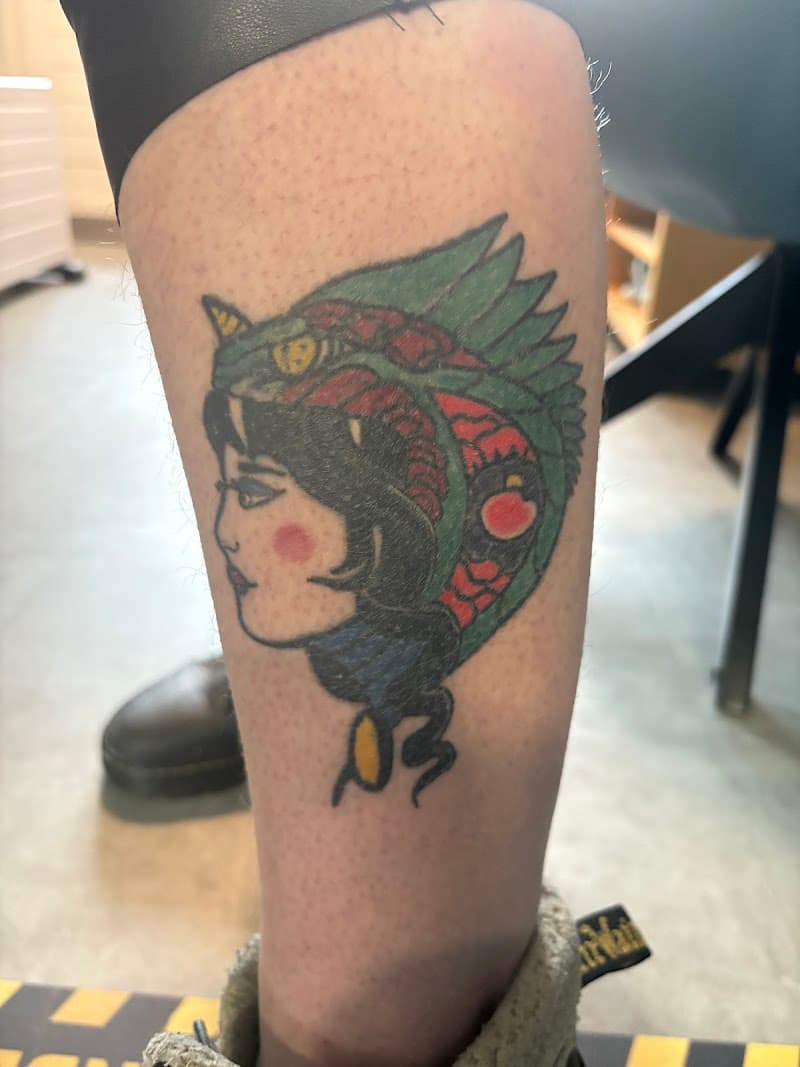 Traditionele tattoo van een vrouwenhoofd met een groene drakenhelm.