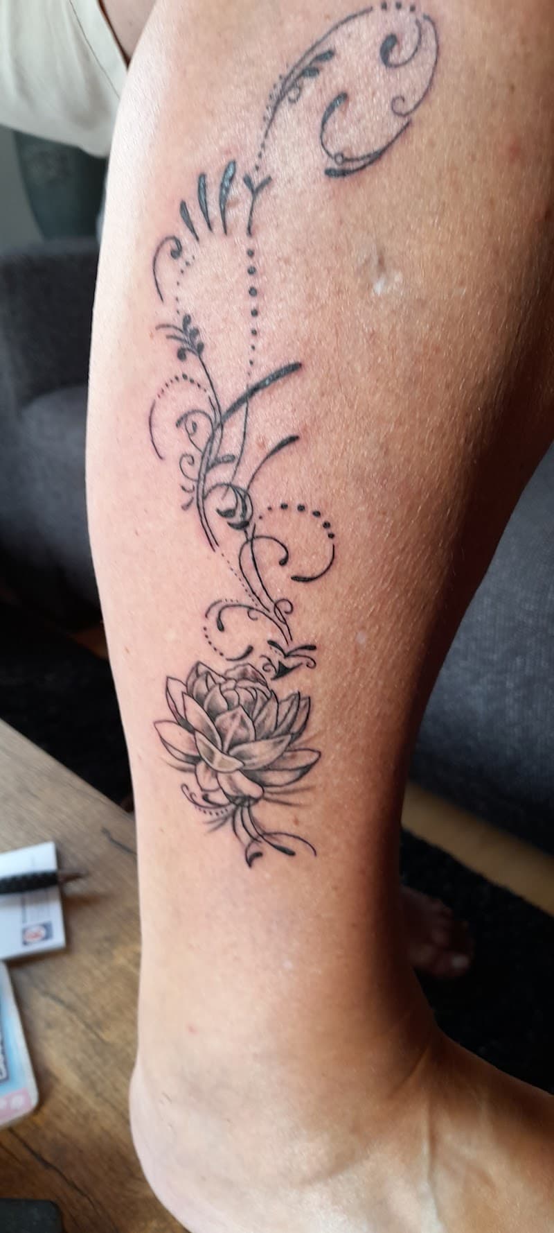 Fineline lotusbloem met sierlijke krullen en stippen op het onderbeen.