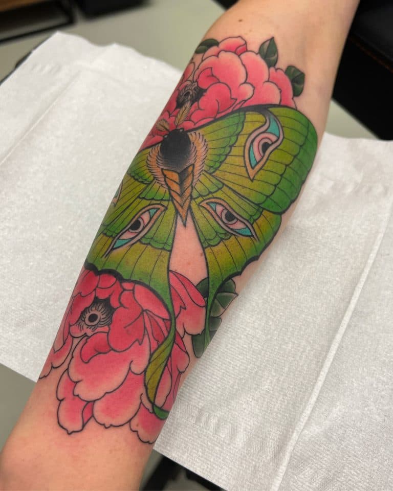 Neo-traditionele groene mot met ogen en roze pioenrozen op onderarm.