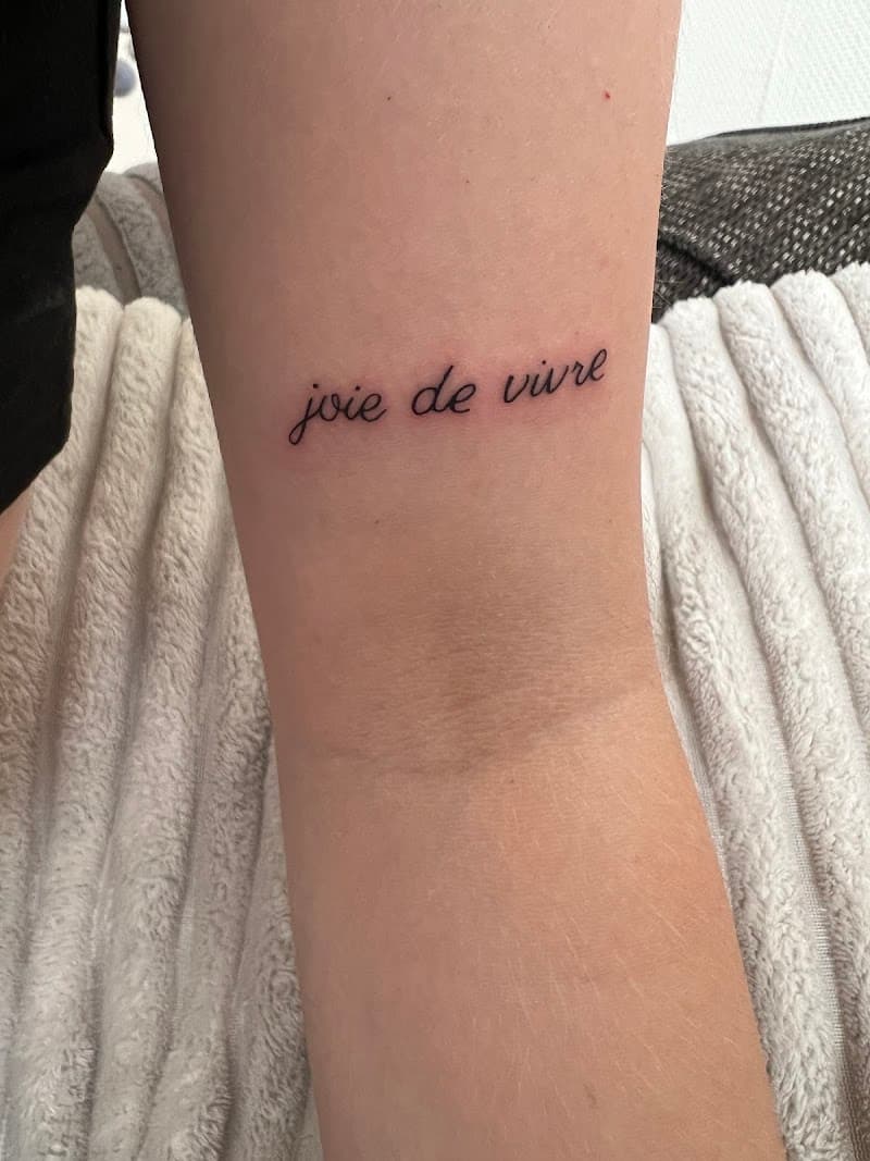 Fineline 'joie de vivre' tekst tattoo op de binnenkant van de arm.