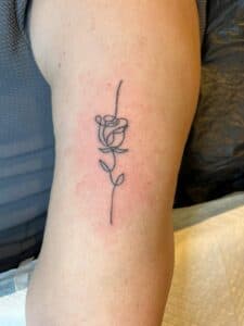 Minimalistische fineline roos tattoo op bovenarm.