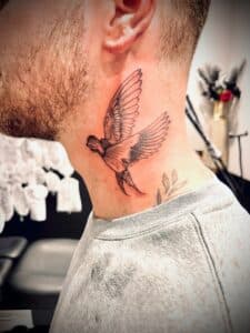 Zwart-wit zwaluw tattoo in de nek, fineline stijl.