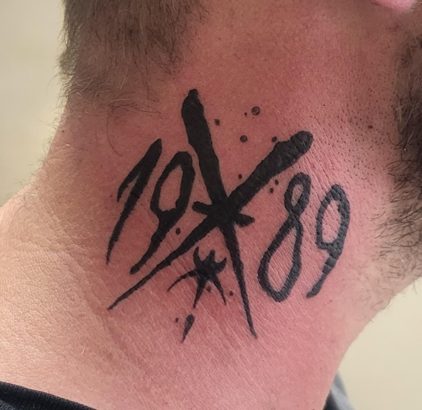 Blackwork tattoo in de nek met het jaartal 1989 en een kruis/ster symbool.