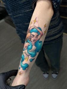 Illustratieve tattoo van een vrouw met blauw haar en sterren op de onderarm.