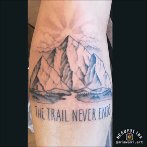 Berglandschap met zon en tekst "THE TRAIL NEVER ENDS" op onderbeen.