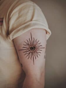Blackwork tattoo van een oog in een zon op de bovenarm.