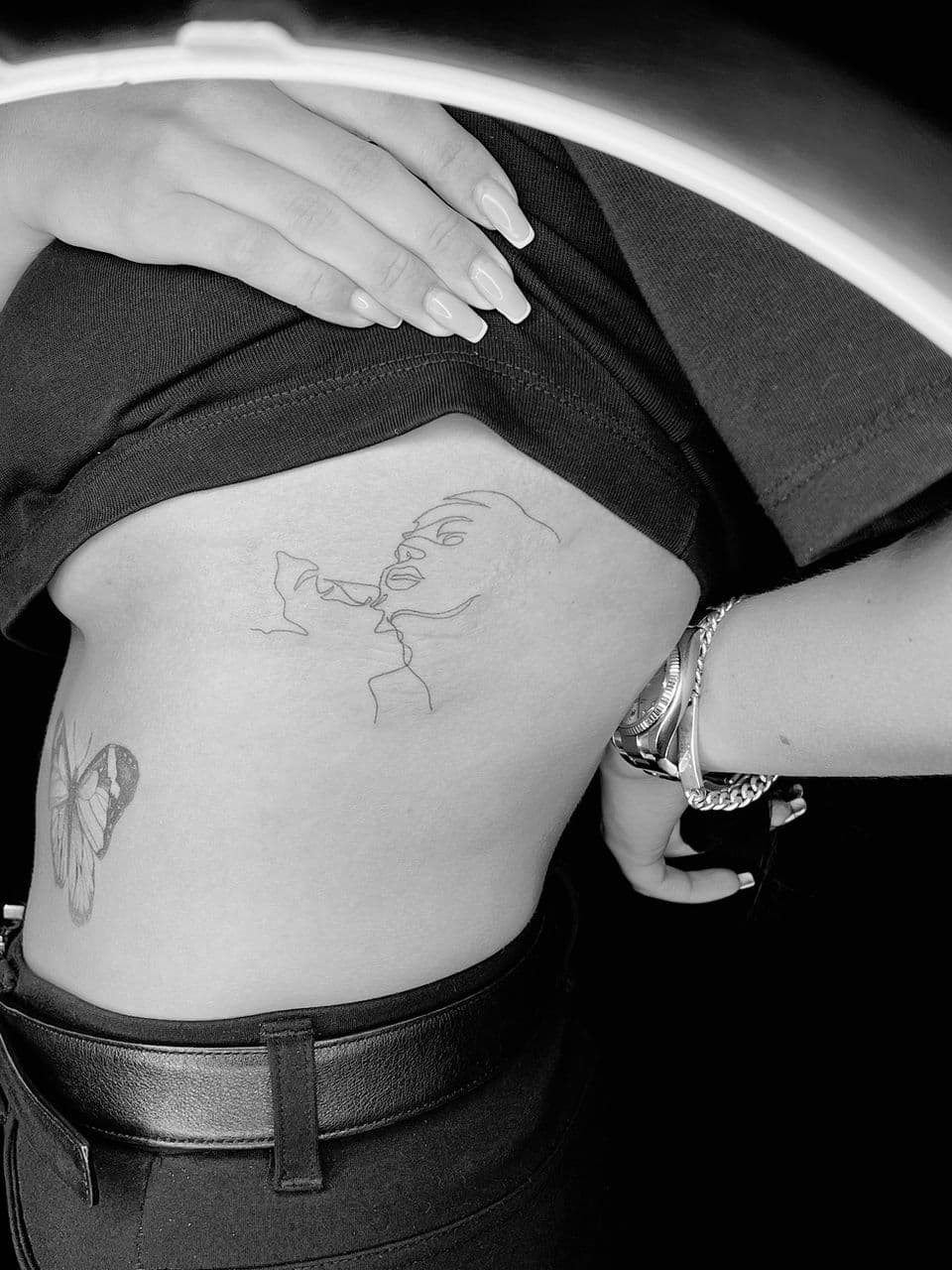 Fineline tattoo van een kus en een vlinder op de ribben.