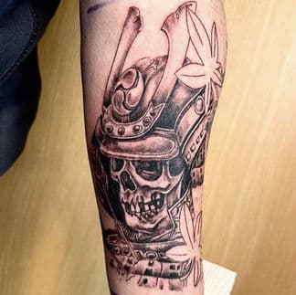 Blackwork tattoo van een samoerai schedel met helm en bladeren.