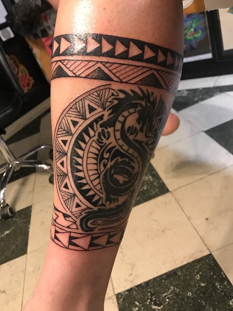 Polynesische stijl tattoo met draak en geometrische banden op onderbeen.