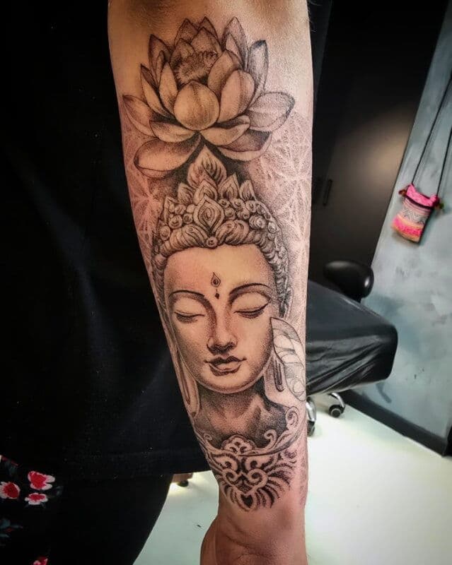 Boeddha hoofd met lotusbloem en mandala achtergrond op onderarm.