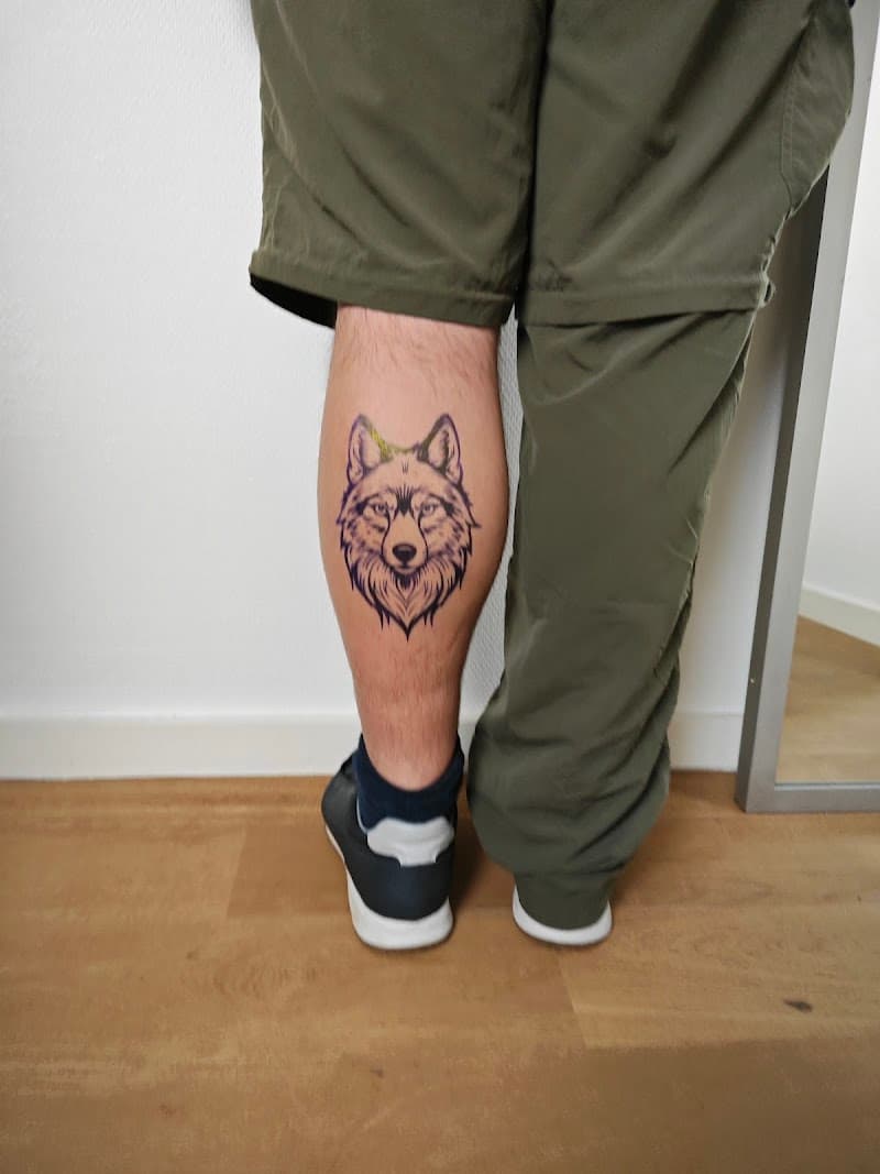 Zwart-wit lijnwerk tattoo van een wolvenkop op de kuit.