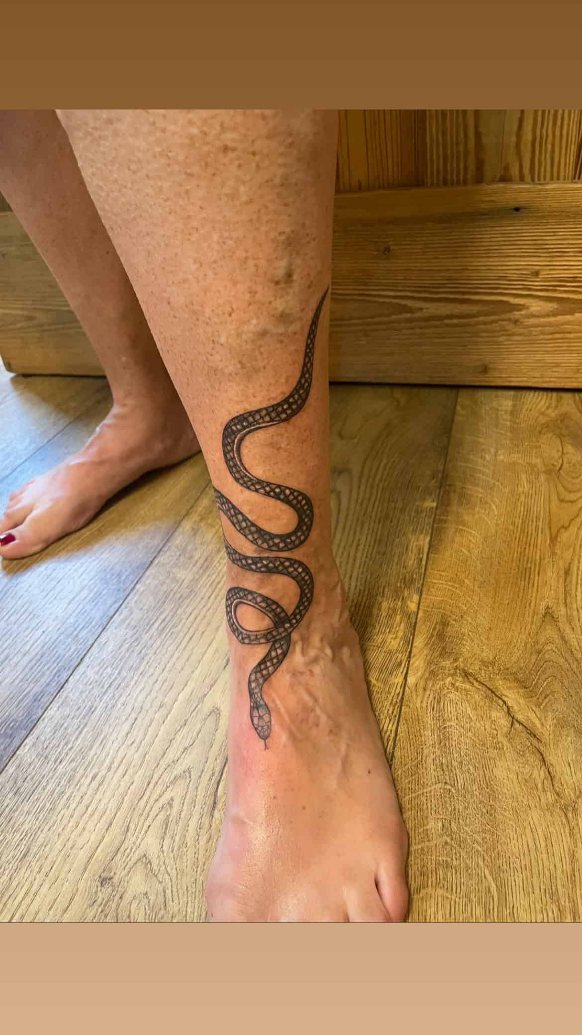 Zwart-wit slang tattoo die om het onderbeen en de voet kronkelt.