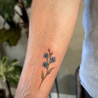 Kleine, realistische vergeet-mij-nietjes tattoo op de onderarm.