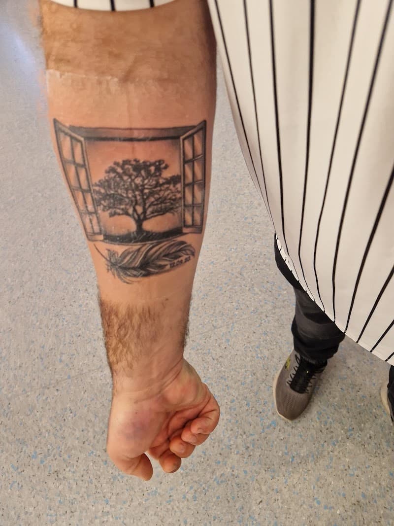 Zwart-wit tattoo van een open raam met een boom en een veer met datum eronder.